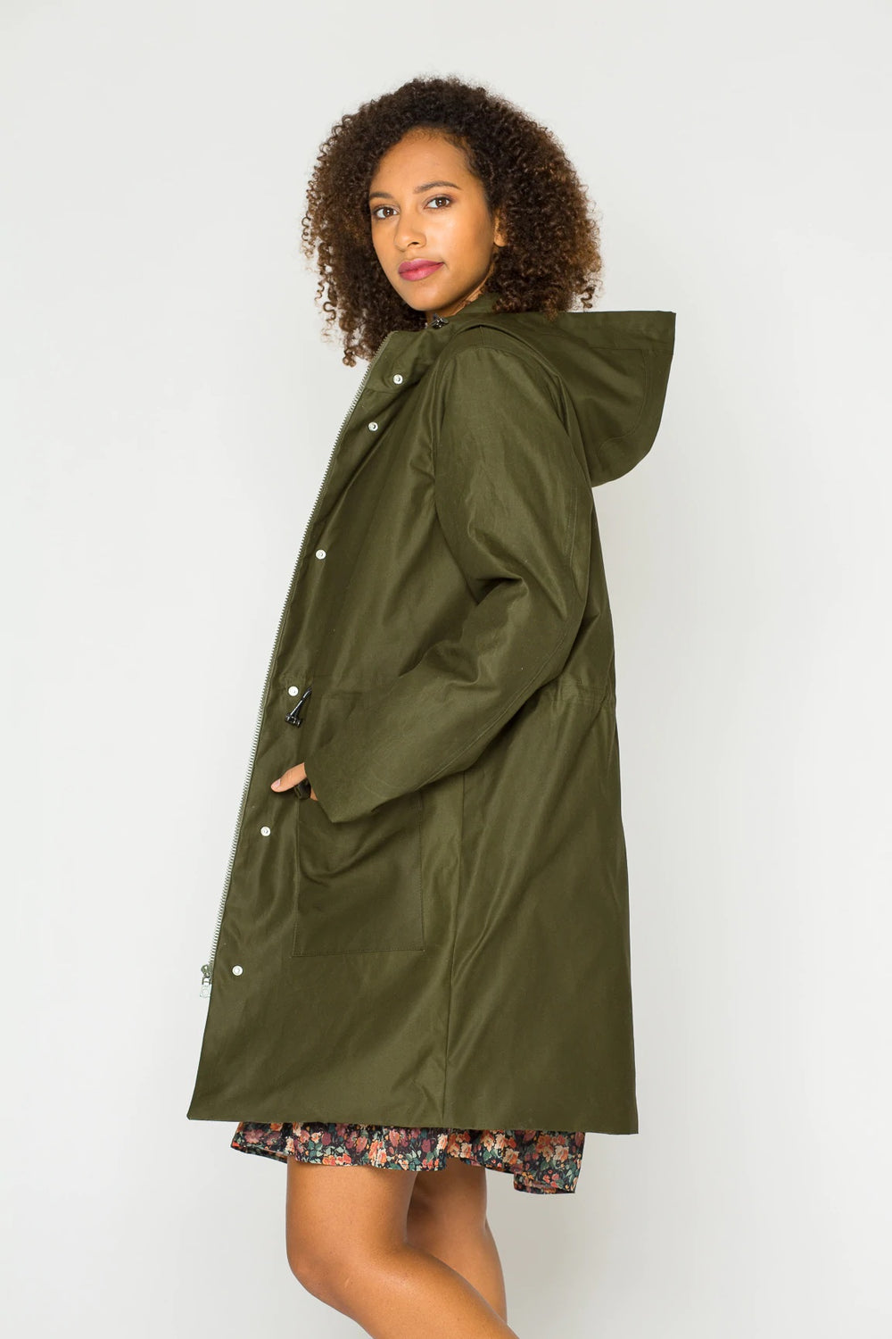Woman wearing the Alma Parka sewing pattern from Bara Studio on The Fold Line. A coat pattern made in oil skin, canvas or denim fabrics, featuring a hood with drawstring, drawstring waist, padded lining, front pocket with flaps, front zipper closure and s