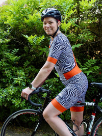 Woman wearing the Triumph Suit sewing pattern from Fehr Trade on The Fold Line. An all-in-one cycling suit pattern made in lycra fabric, featuring short sleeves, no side seams, front and back princess seams, banded shorts hem, front zip fastener, four bac