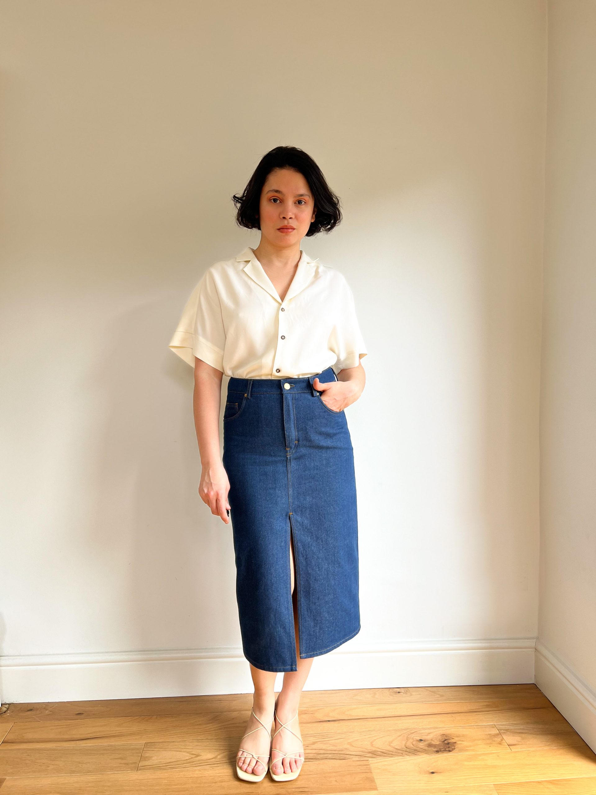 Woman wearing the Anna Skirt sewing pattern from Bella Loves Patterns on The Fold Line. A classic denim skirt pattern made in denim, cotton twill, corduroy, or linen fabric, featuring a fitted straight silhouette, high waist, waistband with belt loops, zi
