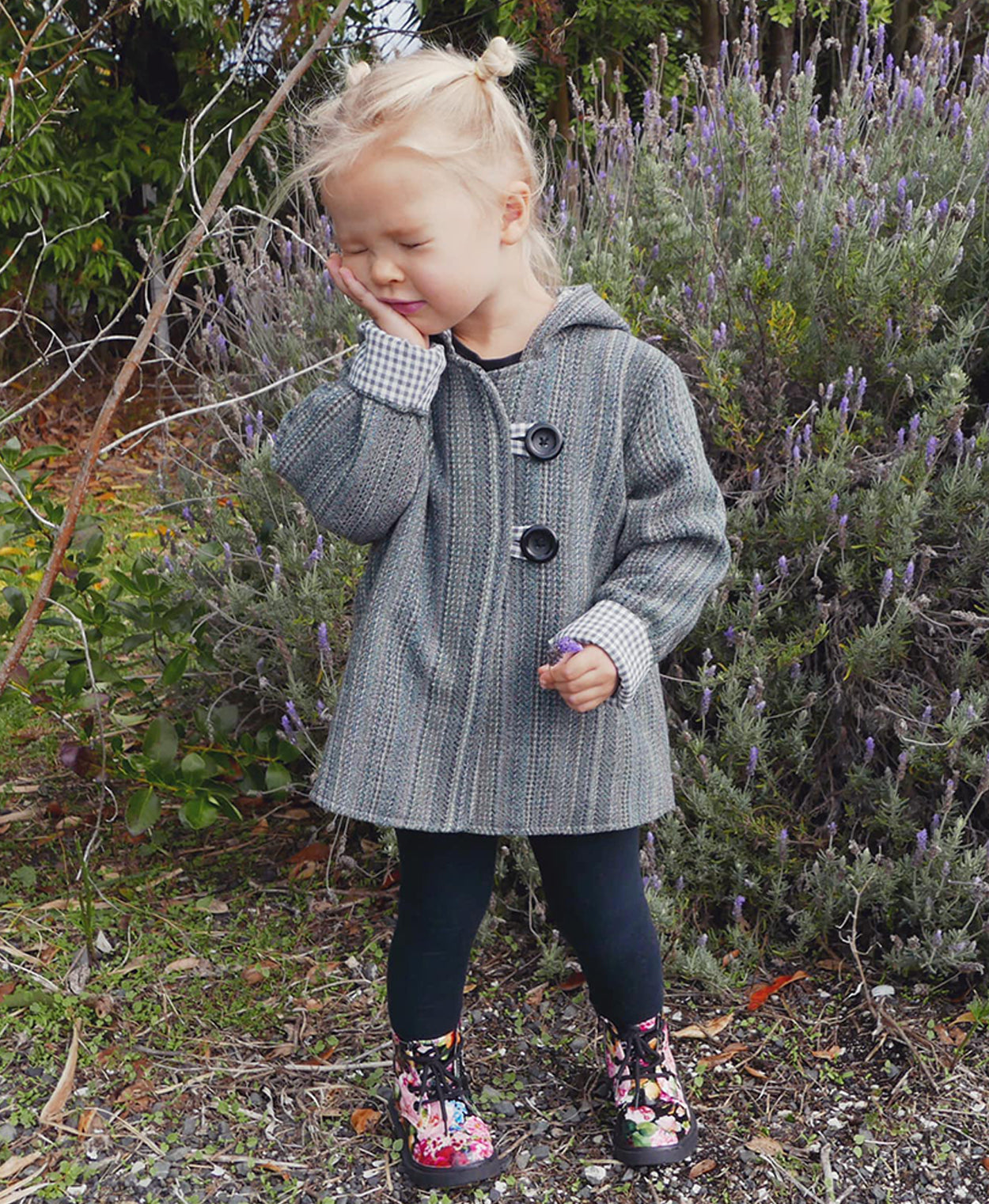 Child wearing the Baby/Child Awhi Coat sewing pattern from Below the Kōwhai on The Fold Line. A coat pattern made in wool, melton cloth or upcycled blnkets fabrics, featuring a cross-over front, gusset style hood, in-seam pockets and button and loop faste