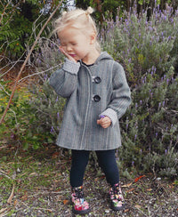 Child wearing the Baby/Child Awhi Coat sewing pattern from Below the Kōwhai on The Fold Line. A coat pattern made in wool, melton cloth or upcycled blnkets fabrics, featuring a cross-over front, gusset style hood, in-seam pockets and button and loop faste
