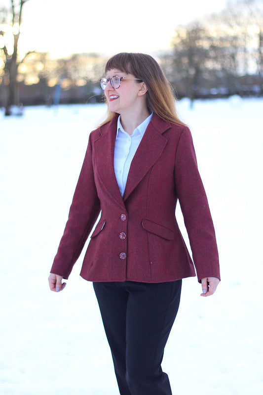 Woman wearing the Barberry Jacket sewing pattern by Charlotte Emma Patterns. A jacket pattern made in suitings, wool, tweed, brocade or cotton fabrics, featuring a shaped slim-fit with a cinched waist, three button closure, pockets and exaggerated hemline