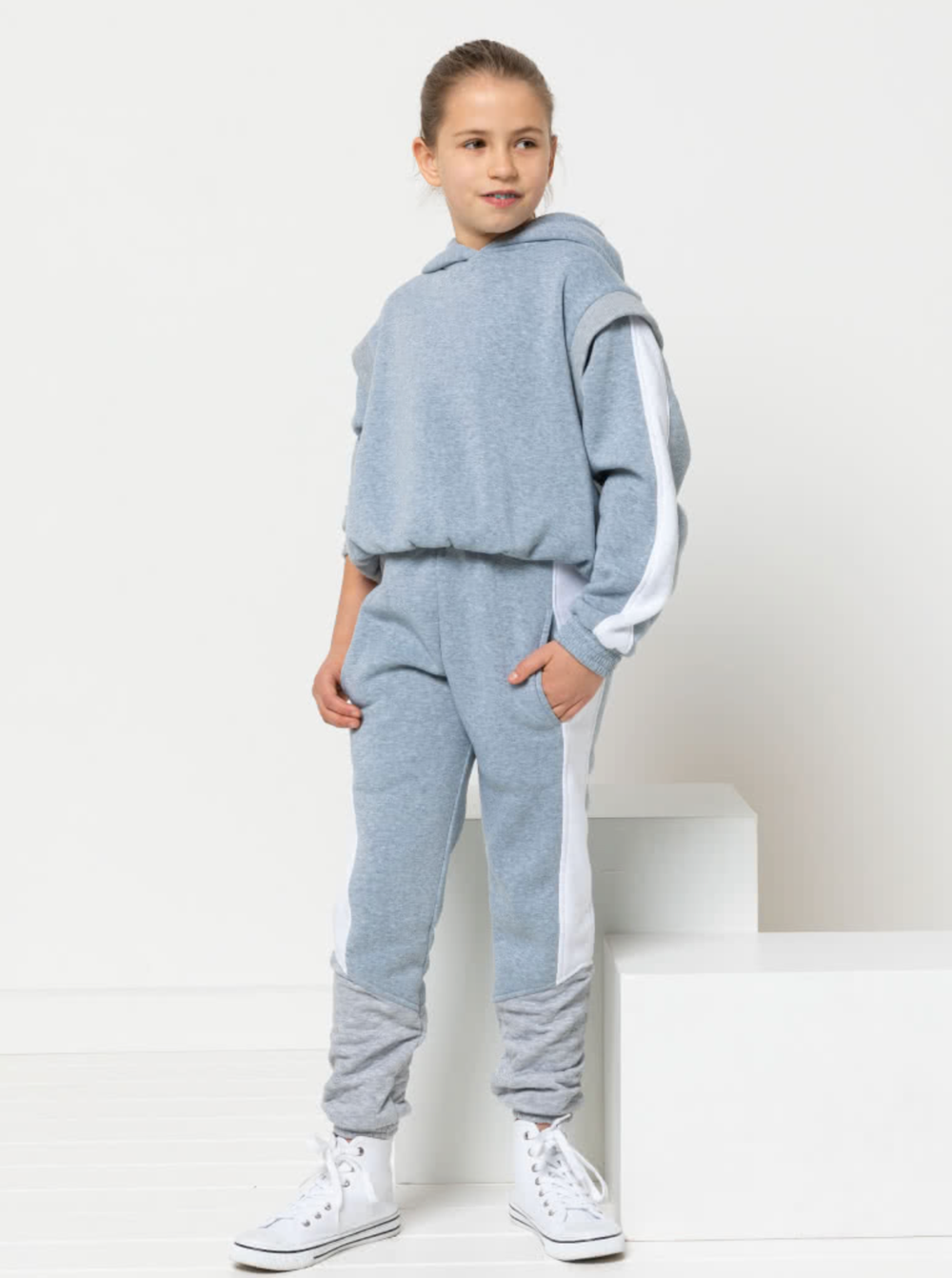 Child wearing the Child/Teen Beckett Sweater sewing pattern from Style Arc on The Fold Line. A hoodie pattern made in fleece, jersey, or sweater knit fabrics, featuring a pull-on style, hood, elasticated waistband and sleeve cuffs, armhole inserts, and sl