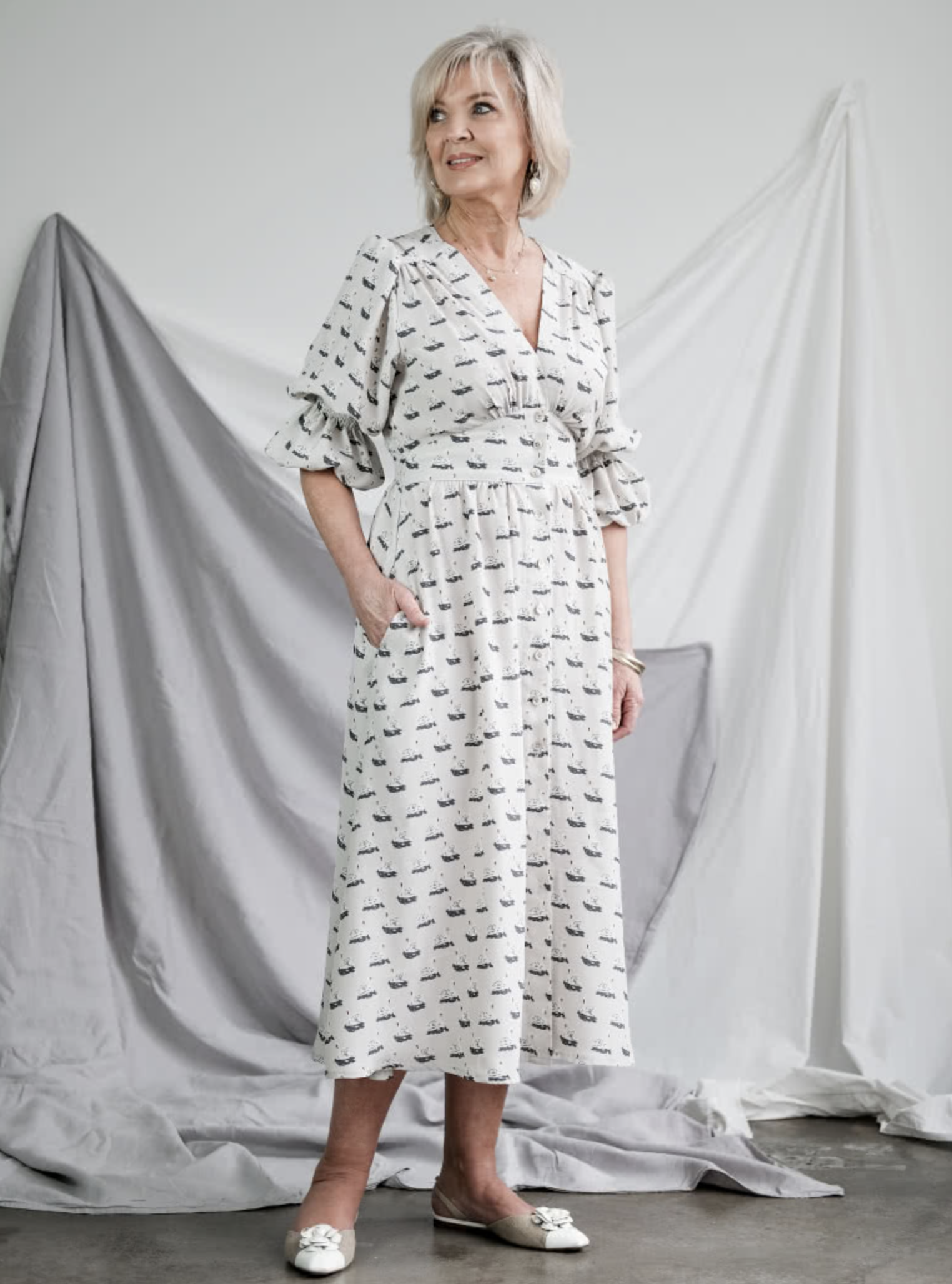 Woman wearing the Belle Woven Dress sewing pattern from Style Arc on The Fold Line. A dress pattern made in crepe, silk or rayon fabrics, featuring a V-neck, front button closure, shirred sleeves with elastic opening, back waist shirring, gathered bodice,