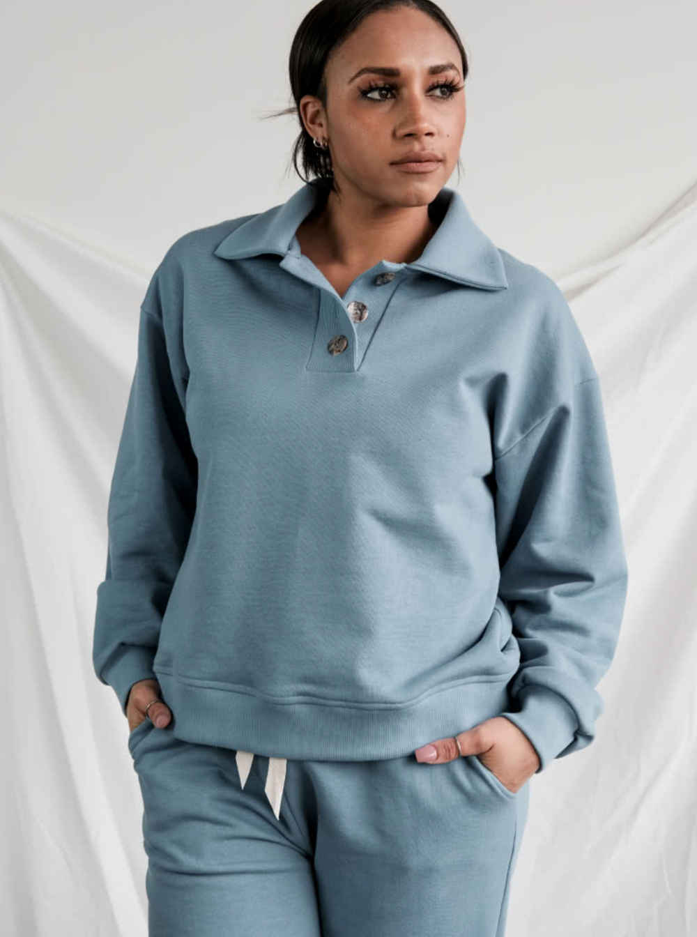 Woman wearing the Bert Knit Top sewing pattern from Style Arc on The Fold Line. A knit top pattern made in unbrushed fleece, fleece or rugby fabrics, featuring a dropped shoulder line, deep armhole, polo style collar and button tab, long sleeves with a sl