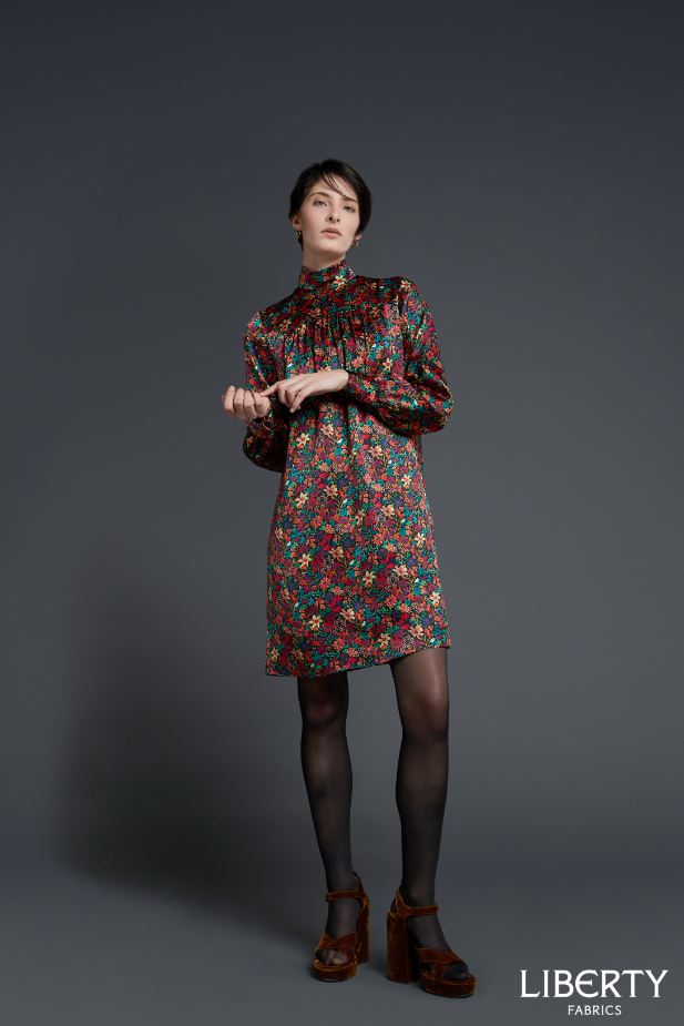 Woman wearing the Bertie Shift Dress sewing pattern by Liberty Sewing Patterns. A dress pattern made in cotton, silk, linen or light velvet fabrics, featuring a high neck, long sleeves with button cuff, back zip closure, relaxed fitting and in-seam pocket
