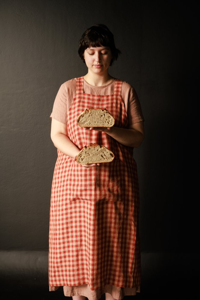 Woman wearing the Betty Apron sewing pattern from Merchant & Mills on The Fold Line. An apron pattern made in linen, linen/cotton blends, denim, and tencel/linen fabrics, featuring a slip over head style, crossover back, and divided patch pocket on the fr