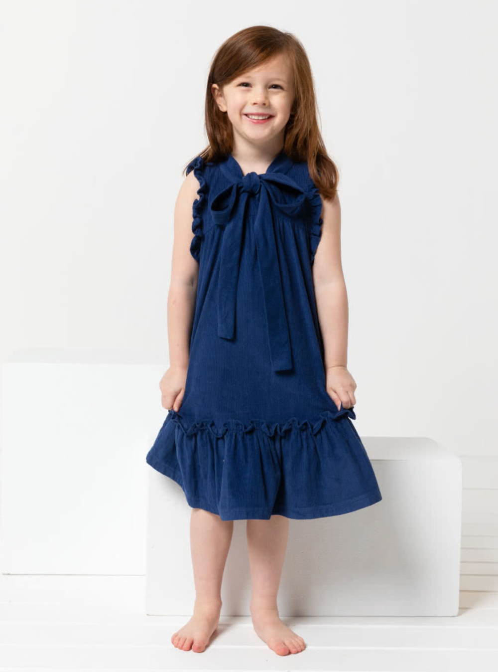 Child wearing the Children's Bonnie Dress sewing pattern from Style Arc on The Fold Line. A dress pattern made in linen, rayon, or cotton fabrics, featuring an A-line swing shape, front and back yokes, gathered armhole and hem frills, neck tie and back ne