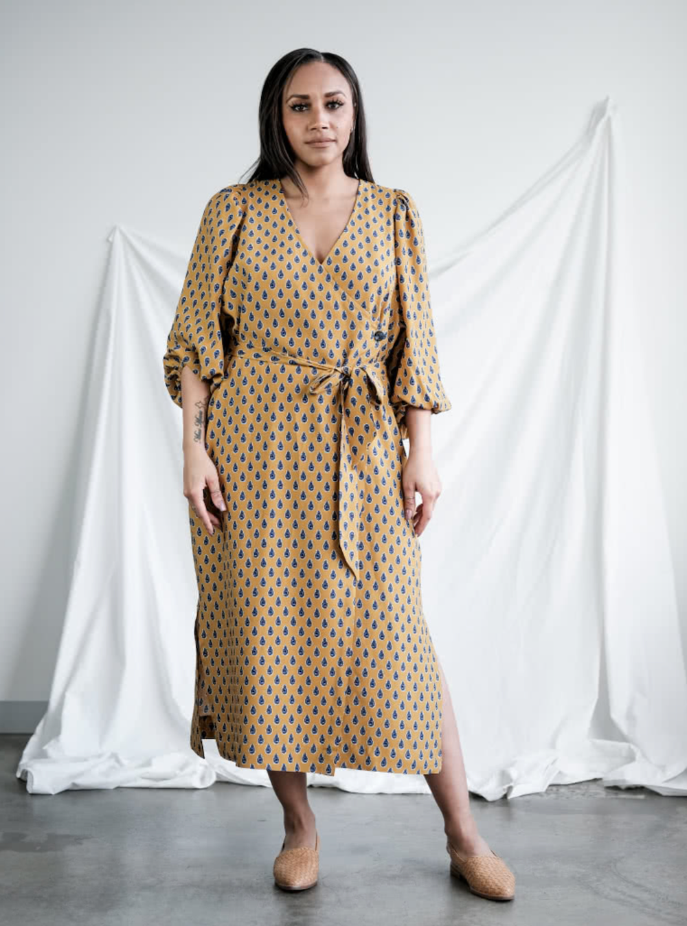 Woman wearing the Brigid Wrap Dress sewing pattern from Style Arc on The Fold Line. A wrap dress pattern made in silk, crepe, viscose or rayon fabrics, featuring a midi length, side button closure, V-neck, deep armhole feature, full sleeve with elastic op