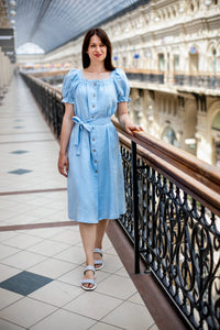 Woman wearing the Brigitte Dress sewing pattern from Kates Sewing Patterns on The Fold Line. A dress pattern made in linen or cotton fabrics, featuring a loose fit, square neckline with ruffle, front placket with buttons, short voluminous sleeves with ela