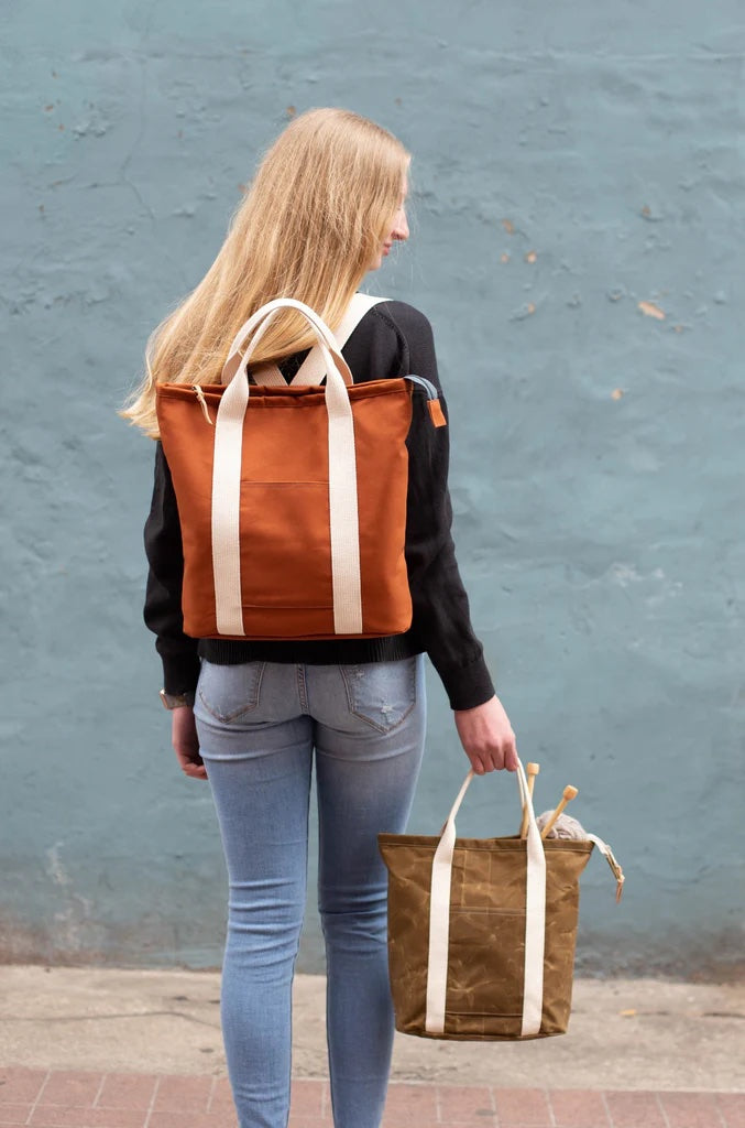 Woman showing the Buckthorn Backpack and Tote sewing pattern from Noodlehead on The Fold Line. A backpack and tote pattern made in canvas or waxed canvas fabrics, featuring a zippered top, front pocket, flat oval base, divided interior pocket, carry handl