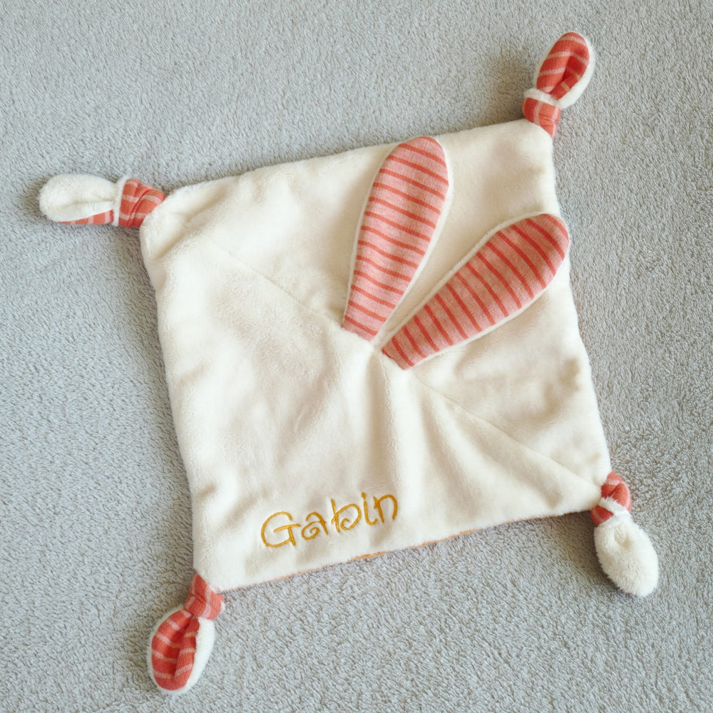 Photo showing the Bunny Lovey Baby Comforter sewing pattern from Petits D'om on The Fold Line. A comforter pattern made in minky or plush fabrics, featuring a square of fabric with bunny ears in the centre and knotted corners.