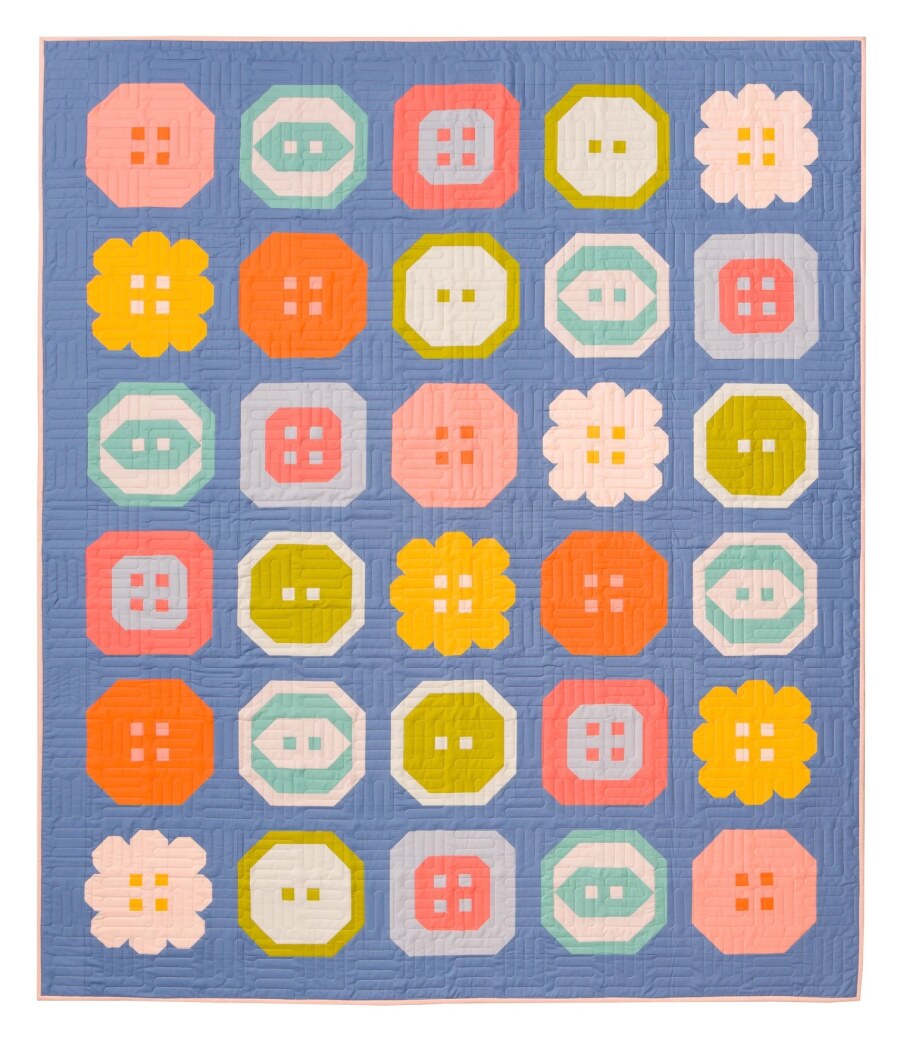 Photo showing the Buttoned Up Quilt sewing pattern from Pen and Paper Patterns on The Fold Line. A quilt pattern made in quilting cotton fabrics, featuring five button blocks arranged randomly throughout the quilt. Plus bonus heart button block, for proje
