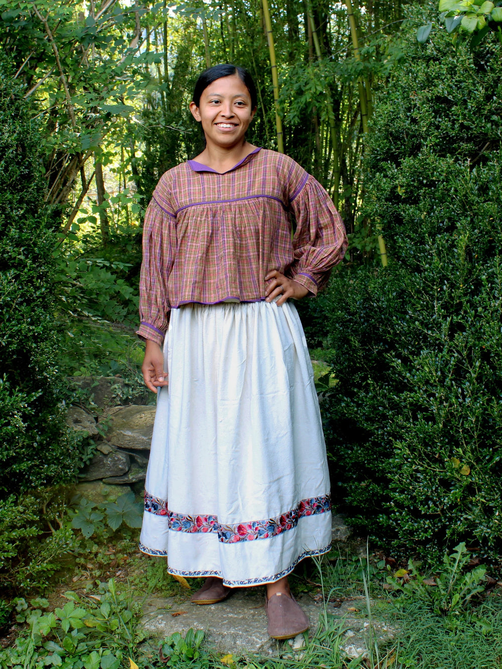 Woman wearing the 125 Huichol Wardrobe sewing pattern from Folkwear on The Fold Line. A blouse and skirt pattern made in cotton, rayon, linen, silk, homespun, muslin, or wool fabric, featuring a short blouse with a full front and back pleated into a yoke and long full sleeves, and a full skirt pleated into a narrow waistband.