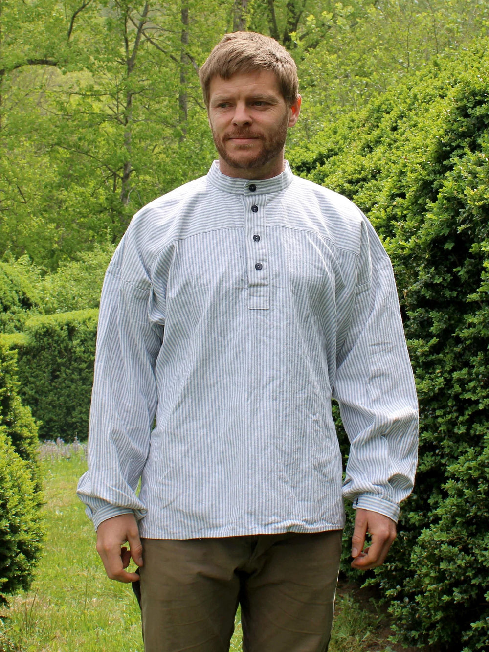 Man wearing the 149 Norwegian Busserull sewing pattern from Folkwear on The Fold Line. A shirt pattern made in cotton, linen, hemp, or wool fabric, featuring a buttoned front placket, underarm gussets, long sleeves, and a half-belt at the back.