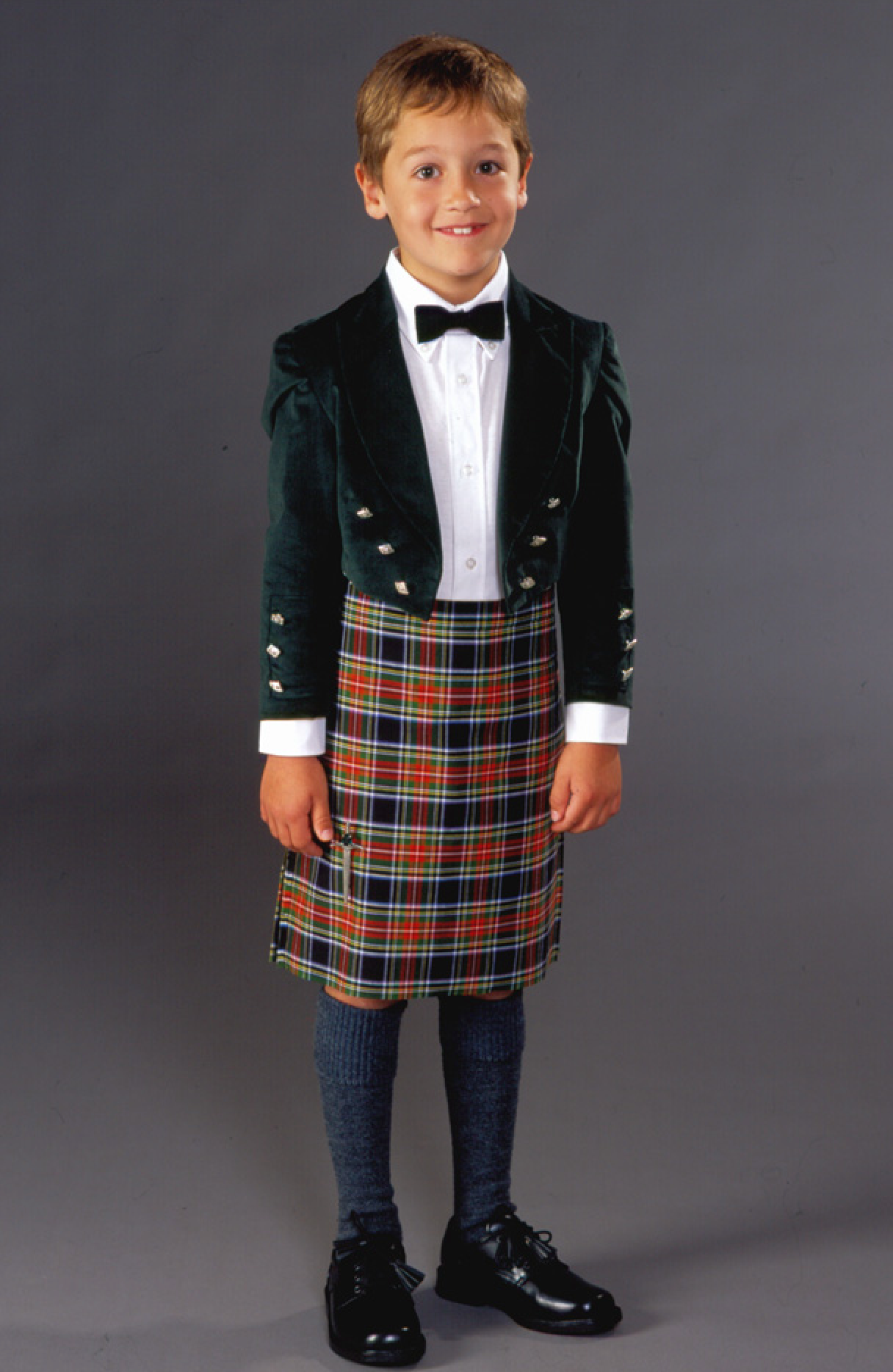 Boy wearing the 154 Child/Teen Scottish Kilt and Jacket sewing pattern from Folkwear on The Fold Line. A kilt and Prince Charlie jacket made in wool fabric, featuring a knee length pleated kilt and jacket with lapels, long sleeves, decorative buttons, and cropped length.