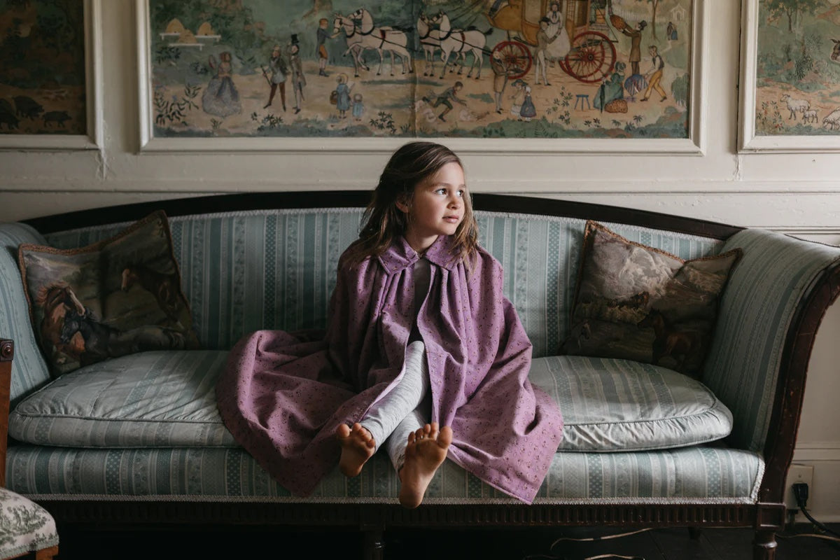 Girl wearing the 208 Children's Kinsale Cloak sewing pattern from Folkwear on The Fold Line. A fully lined cloak pattern made in velvet, corduroy, denim, wool, heavyweight silk, or microfibre fabric, featuring a wide collar and curved hem.