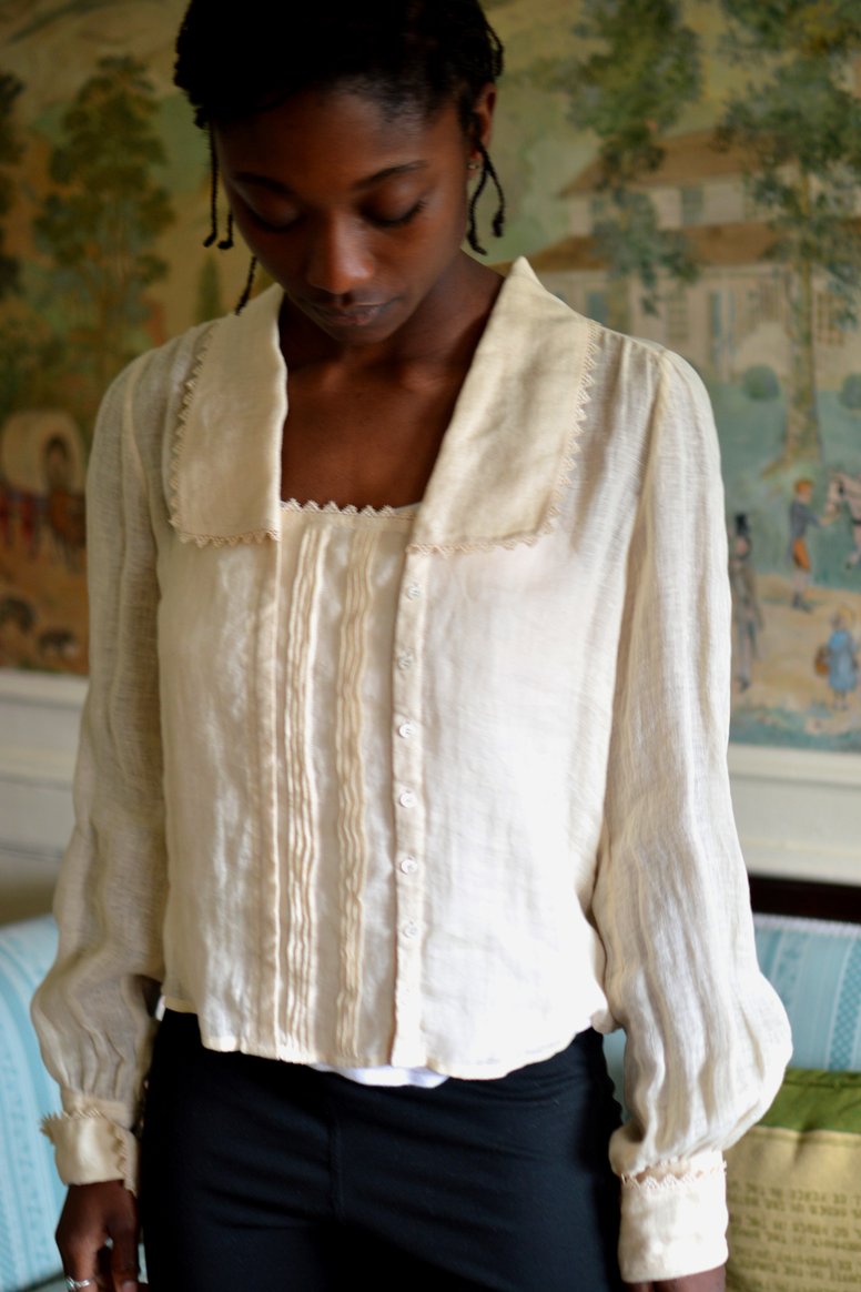 Woman wearing the 210 Armistice Blouse sewing pattern from Folkwear on The Fold Line. A blouse pattern made in gauze, batiste, voile, georgette, light cotton, silk, or rayon fabric, featuring a deep rectangular neckline, long collar, centre panel with pintucks, tiny buttons, and long set-in sleeves gathered into wide turned-back cuffs.