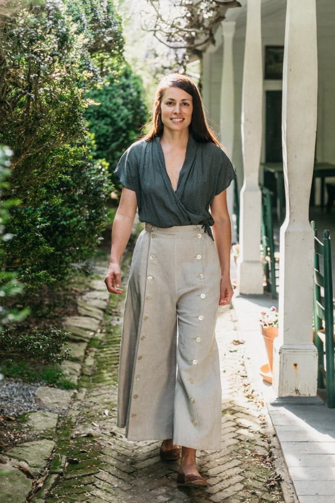 Woman wearing the 231 Big Sky Riding Skirt sewing pattern from Folkwear on The Fold Line. A culottes pattern made in cotton poplin, denim, gabardine, corduroy, linen, wool, or suiting weight silk fabric, featuring a movable front panel that buttons to either side for a skirt or pant effect, side seam pockets, and ankle length.