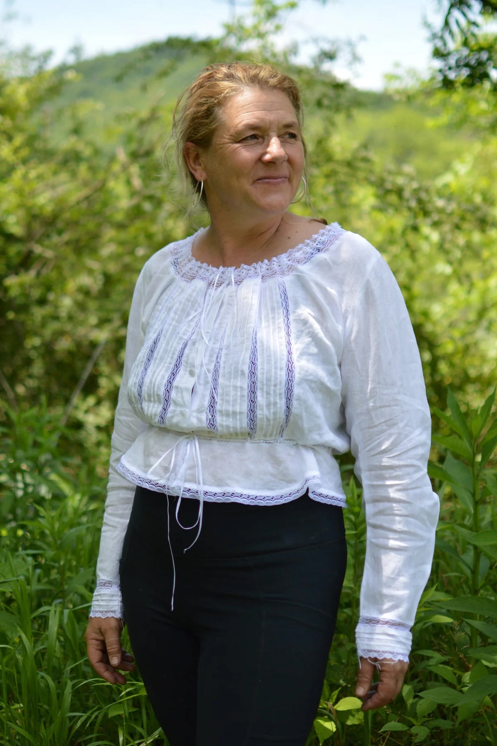 Woman wearing the 234 Cameos sewing pattern from Folkwear on The Fold Line. A top pattern made in fine cottons or blends such as lawn, batiste, broadcloth, muslin, or silk fabric, featuring a scoop neckline with a drawstring and edging lace, tucks and inserted lace on the bodice, long sleeves, a drawstring at the waist, and a peplum.