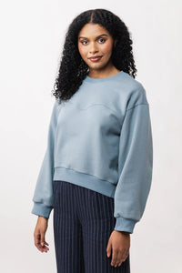 Woman wearing the Aalto Sweatshirt sewing pattern from Named on The Fold Line. A top pattern made in sweatshirt jersey, terry, or light neoprene fabric, featuring a relaxed shape, round neckline, wavy front seam, forward-curving side seams, long sleeves, and a curved hem.