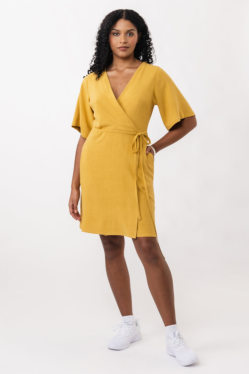 Woman wearing the Aaria Mini Wrap Dress sewing pattern from Named on The Fold Line. A wrap dress pattern made in viscose, viscose blends, soft cotton, or linen fabric, featuring a deep V-neckline, elbow length T-shirt sleeves, thin wrap ties, side pockets, and above knee length.
