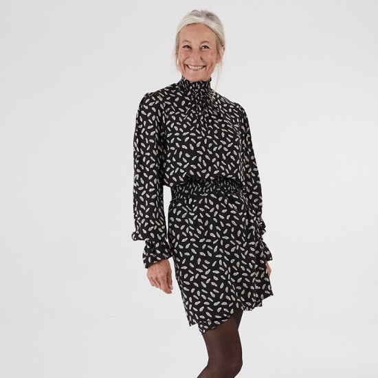 Woman wearing the Alhambra Dress sewing pattern from Coralie Bijasson on The Fold Line. A dress pattern made in cotton, voile, crepe, or viscose fabric, featuring a shirred funnel neck with buttons at the back, long puff sleeves with a shirred cuff, a removable belt, side seam pockets, and mini length.