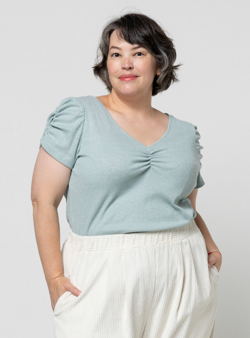 Woman wearing the Alice Knit Top sewing pattern from Style Arc on The Fold Line. A tee pattern made in knit fabric, featuring a V-neckline, elasticated ruching at the centre front, and ruched short sleeves.