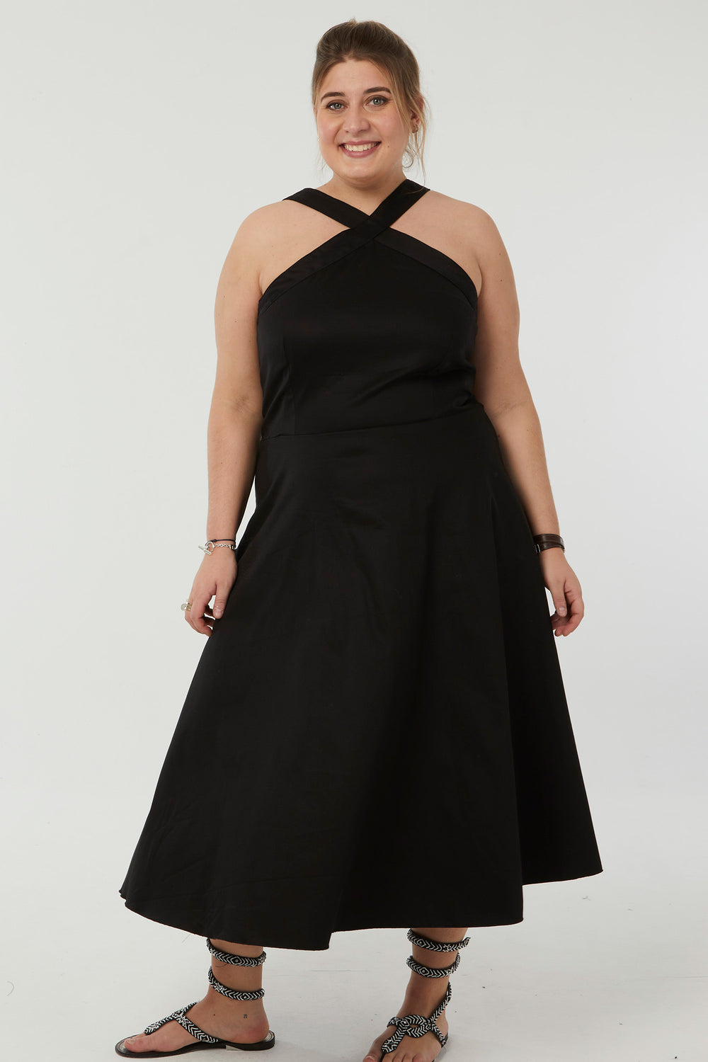 Woman wearing the Aliocha Dress sewing pattern from Coralie Bijasson on The Fold Line. A dress pattern made in cotton satin, linen/viscose, linen, or viscose crepe fabric, featuring a fitted bodice, crossed straps at the front, and midi length.