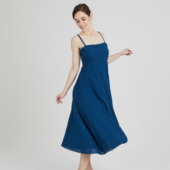 Woman wearing the Anastasia Dress sewing pattern from Coralie Bijasson on The Fold Line. A dress pattern made in cotton, voile, crepe, or viscose fabric, featuring a fitted bodice, thin straps, high waist, flared skirt, and midi length.
