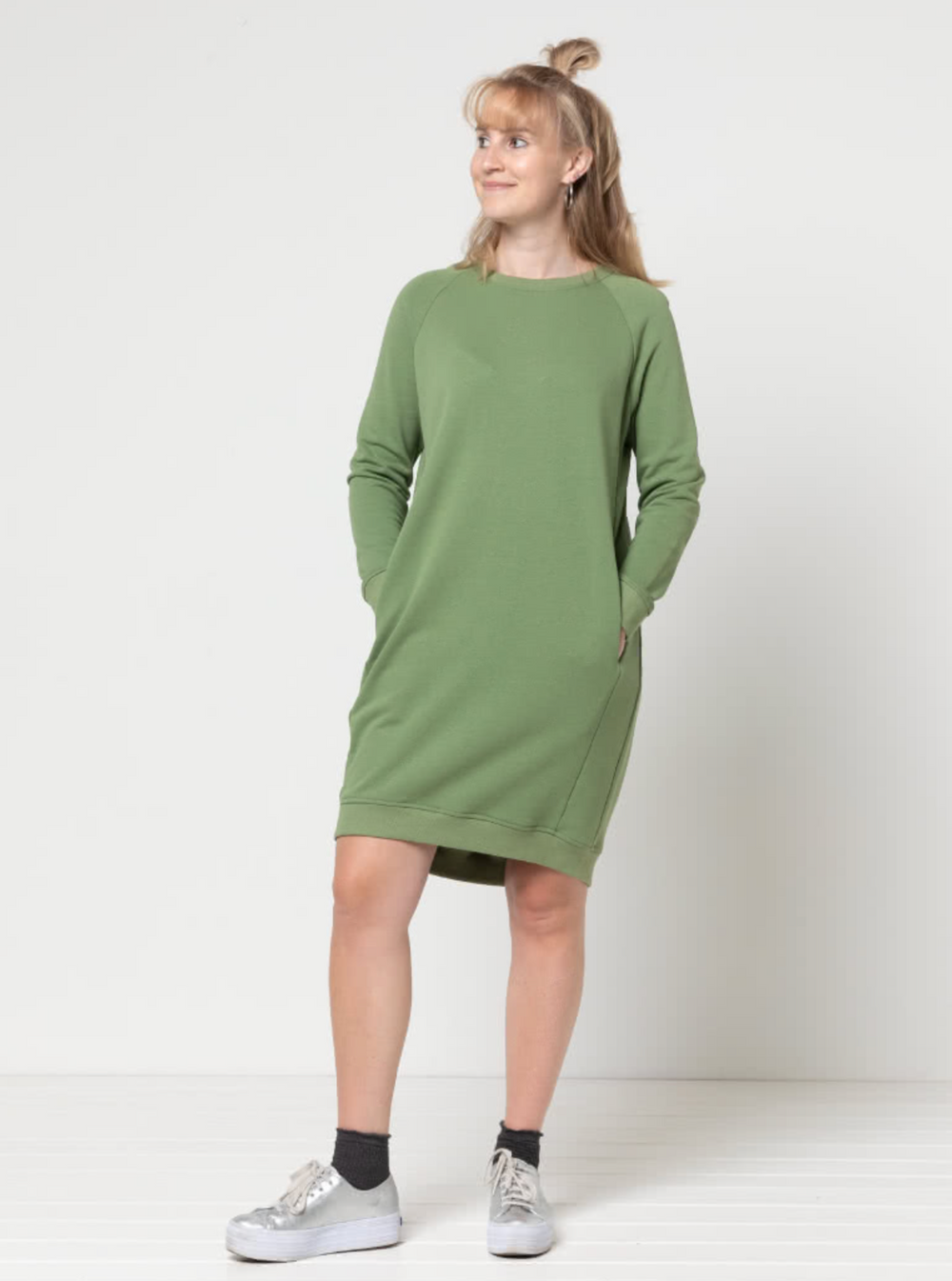 Woman wearing the Anderson Knit Dress sewing pattern from Style Arc on The Fold Line. A sweatshirt dress pattern made in French terry, fleece, or rugby knit fabric, featuring a crew neck, raglan sleeves, side front panels, in-seam pockets, and a slight high-low hemline.
