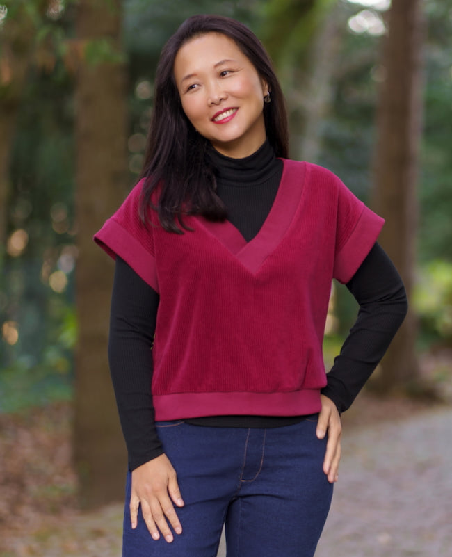 Woman wearing the Andorra Vest sewing pattern from Itch to Stitch on The Fold Line. A sleeveless top pattern made in knit fabric, featuring a relaxed fit, deep V-neckline, armhole bands, and a bottom band.
