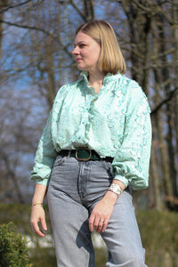 Woman wearing the Anoushka Blouse sewing pattern from Lenaline Patterns on The Fold Line. A shirt pattern made in cotton poplin, cotton twill, linen, tencel, denim, cotton twill, chino, flannel, viscose, or silk fabric, featuring a relaxed fit, high collar, gathers at the front and back, a gathered ruffle, button placket, and long sleeves with cuffs.