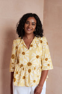 Woman wearing the April Blouse sewing pattern from NH Patterns on The Fold Line. A top pattern made in lightweight cotton, cotton chambray, linen, tencel, or rayon/viscose fabric, featuring neck ties, 3/4 length sleeves with pintucks, and a gathered peplum.