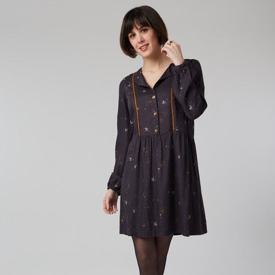Woman wearing the Ariane Dress sewing pattern from Coralie Bijasson on The Fold Line. A dress pattern made in viscose crepe, linen, light wool, chambray or cotton fabric, featuring buttons at the front, piped princess seams, long sleeves with elastic at the wrist, and a short gathered skirt. 