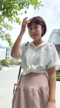 Woman wearing the Arles Top sewing pattern from Sewing Therapy on The Fold Line. A blouse pattern made in linen, double gauze, rayon, viscose, tencel, or light chambray fabric, featuring a rounded collar, button front, gathers at the shoulders and back yoke, front tie, and short sleeves.