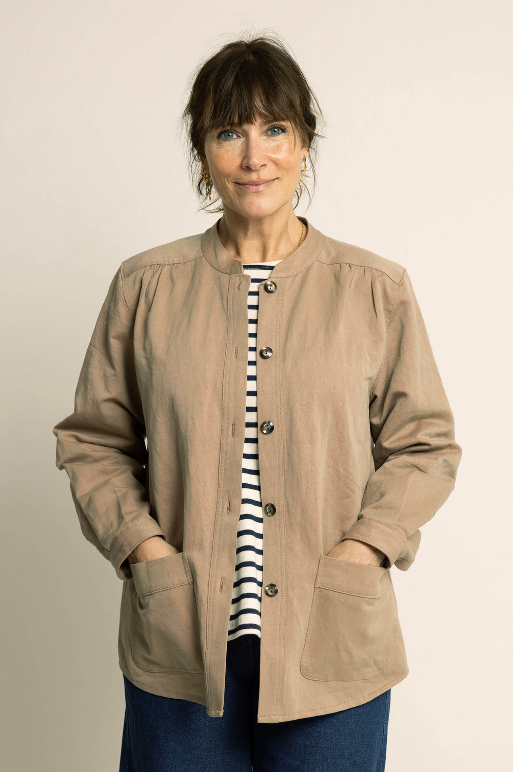 Woman wearing the Artist Jacket sewing pattern from Wardrobe by Me on The Fold Line. A jacket pattern made in cotton, linen, denim, flannel, corduroy, or light wool fabric, featuring a band collar, front button placket, front and back gathers, long sleeves with cuffs, and patch pockets. 