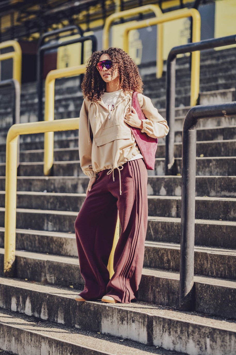 Woman wearing the Arya Trousers sewing pattern from Fibre Mood on The Fold Line. A jogging trousers pattern made in jersey, French terry, scuba, punto di Roma, or sweater fabric, featuring a relaxed fit, elastic waist, side pockets, back yoke, and pintucked stripe detail at the sides.