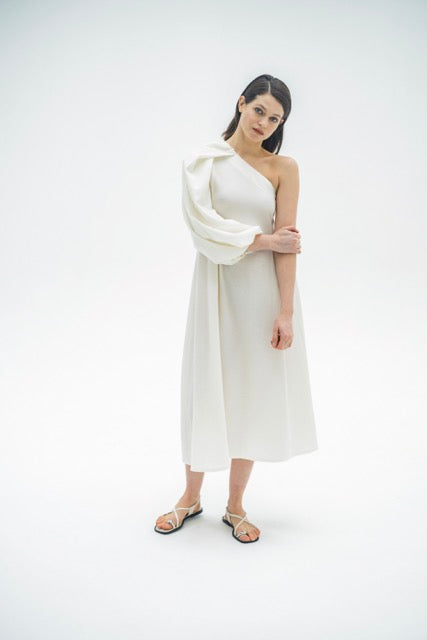 Woman wearing the Ashley Dress sewing pattern from Fibre Mood on The Fold Line. A one-shoulder dress pattern made in poplin, raw silk, nylon, cotton twill, denim, linen, tencel or double gauze fabric, featuring an A-line silhouette, midi length, and statement balloon sleeve.