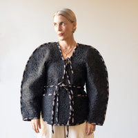 Woman wearing the August Jacket sewing pattern from Pattern Fantastique on The Fold Line. A jacket pattern made in pre-quilted fabric, wool, denim, canvas, or duck cloth fabric, featuring an oversized sculptural silhouette, contrast binding, V-neckline, ties, and pockets.