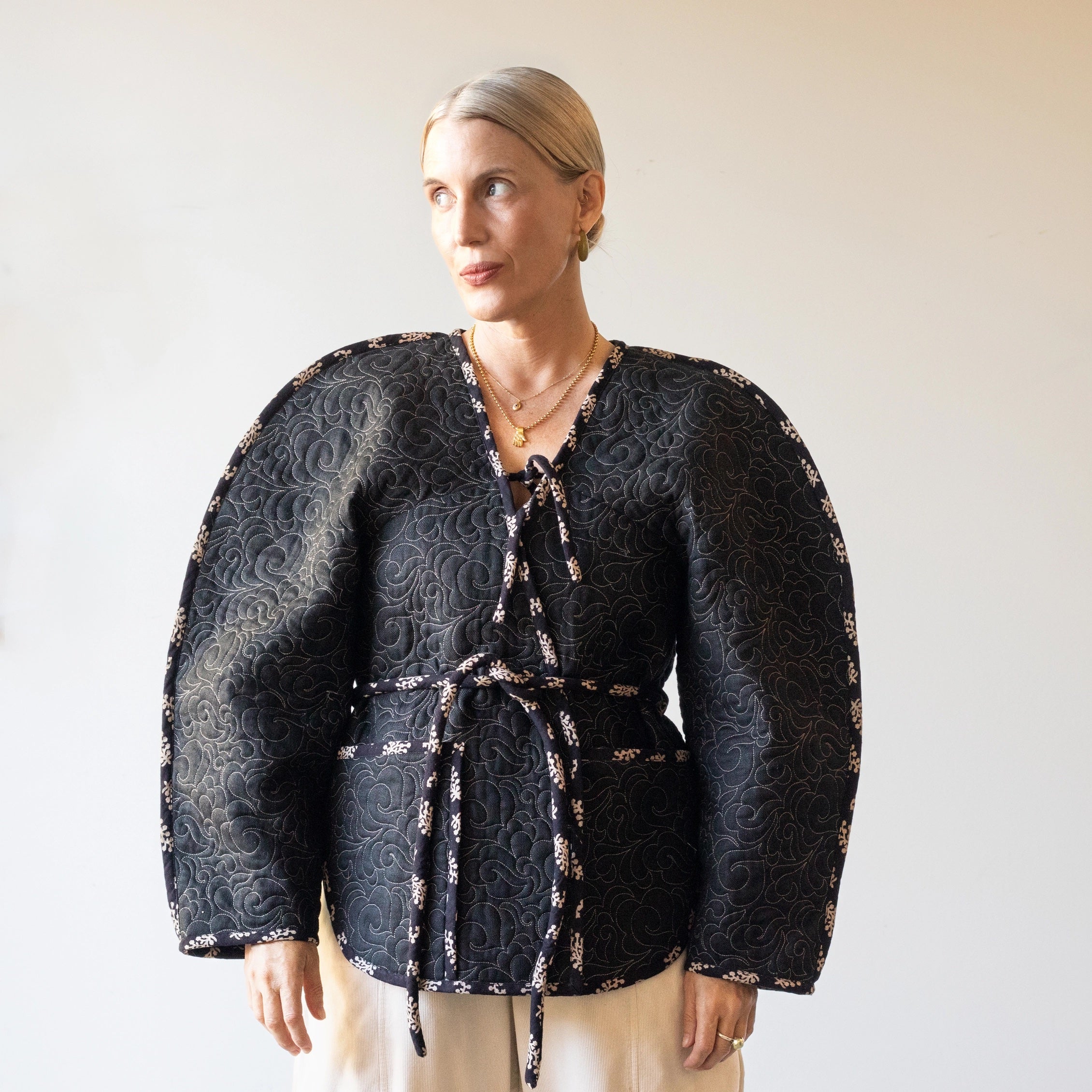Woman wearing the August Jacket sewing pattern from Pattern Fantastique on The Fold Line. A jacket pattern made in pre-quilted fabric, wool, denim, canvas, or duck cloth fabric, featuring an oversized sculptural silhouette, contrast binding, V-neckline, ties, and pockets.