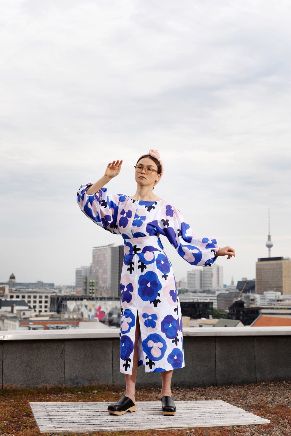 Woman wearing the Aurelia Dress sewing pattern from TAUKO on The Fold Line. A dress pattern made in cotton, poplin, or shirting fabric, featuring a rounded neckline, long voluminous statement sleeves, a self fabric belt, front slit, and midi length.