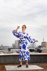Woman wearing the Aurelia Dress sewing pattern from TAUKO on The Fold Line. A dress pattern made in cotton, poplin, or shirting fabric, featuring a rounded neckline, long voluminous statement sleeves, a self fabric belt, front slit, and midi length.