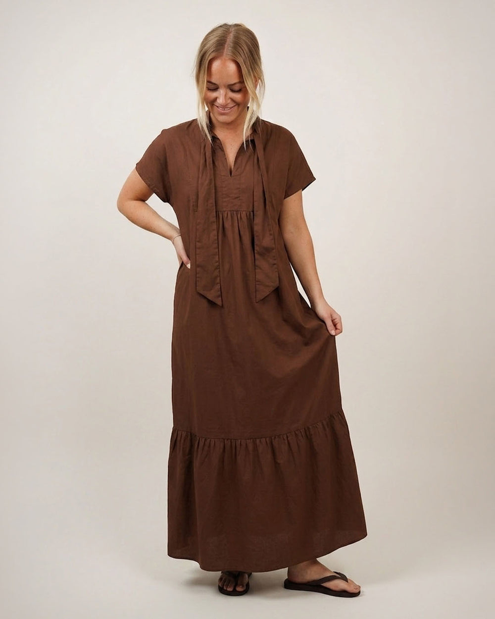 Woman wearing the Aurora Kaftan Dress sewing pattern from Wardrobe by Me on The Fold Line. A dress pattern made in cotton, viscose, silk, linen, or double gauze fabric, featuring a loose fit, collar with a front tie, short grown-on sleeves, ruffle hem, and above ankle length.