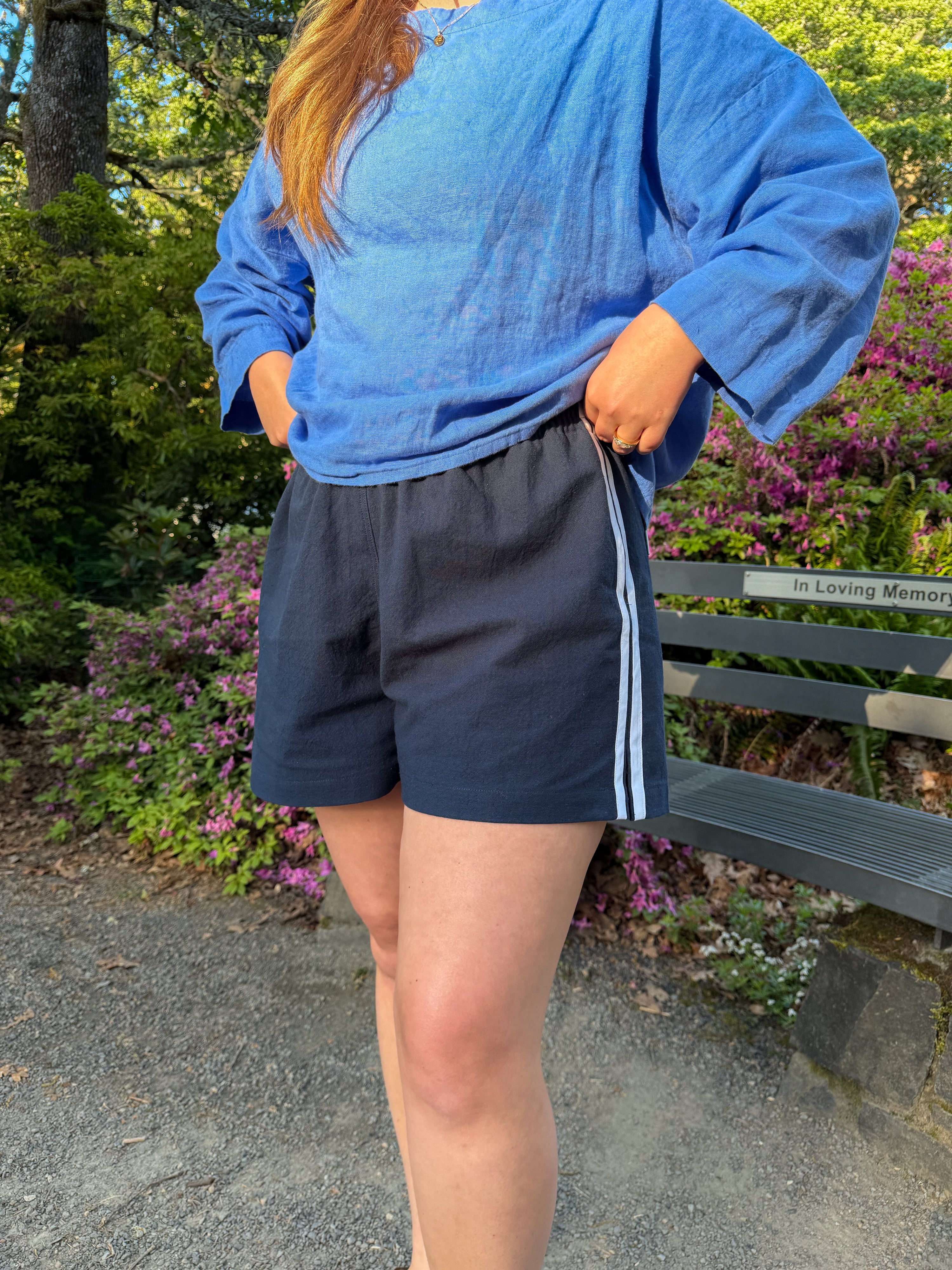Woman wearing the Avenue Shorts sewing pattern from Syd Graham Patterns on The Fold Line. A shorts pattern made in cotton, linen, ripstop nylon, sweatshirt fleece, or French terry fabric, featuring a moderately high rise, subtle A-line silhouette, elastic waistband, and side stripes.