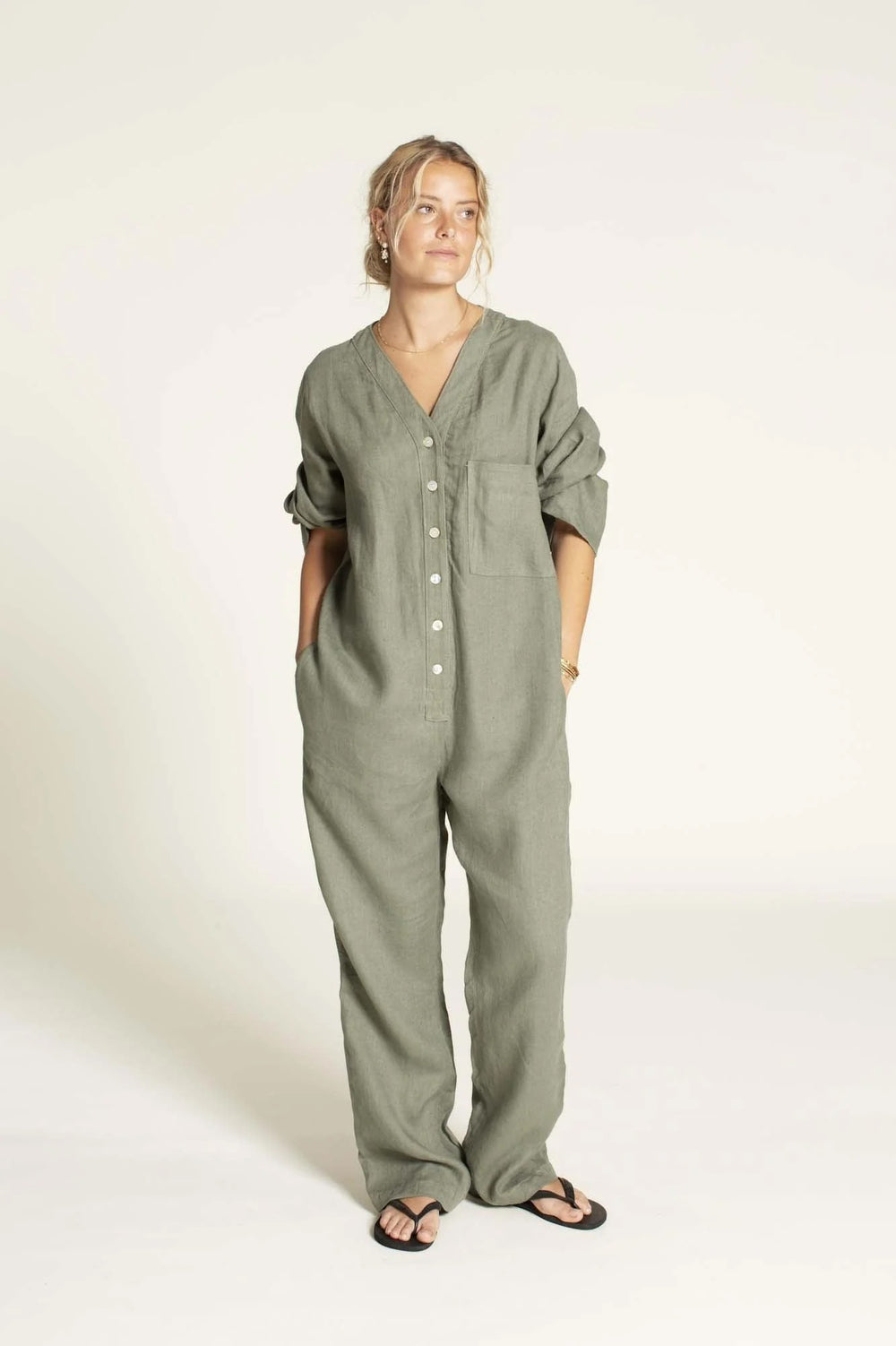 Woman wearing the Aviator Jumpsuit sewing pattern from Wardrobe by Me on The Fold Line. A jumpsuit pattern made in linen, cotton, denim, canvas, or twill fabric, featuring a V-neckline, button front, long sleeves with sleeve tabs, pockets, and a relaxed fit.