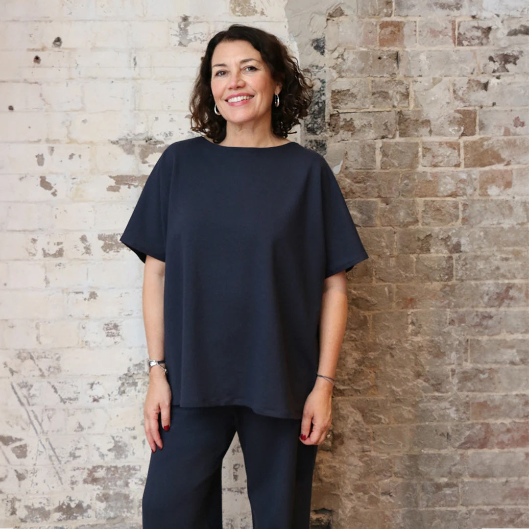 Woman wearing the Avoca Top sewing pattern from Tessuti Fabrics on The Fold Line. A top pattern made in knit fabric, featuring a relaxed fit, high boat neckline, short grown-on sleeves, and hip length.