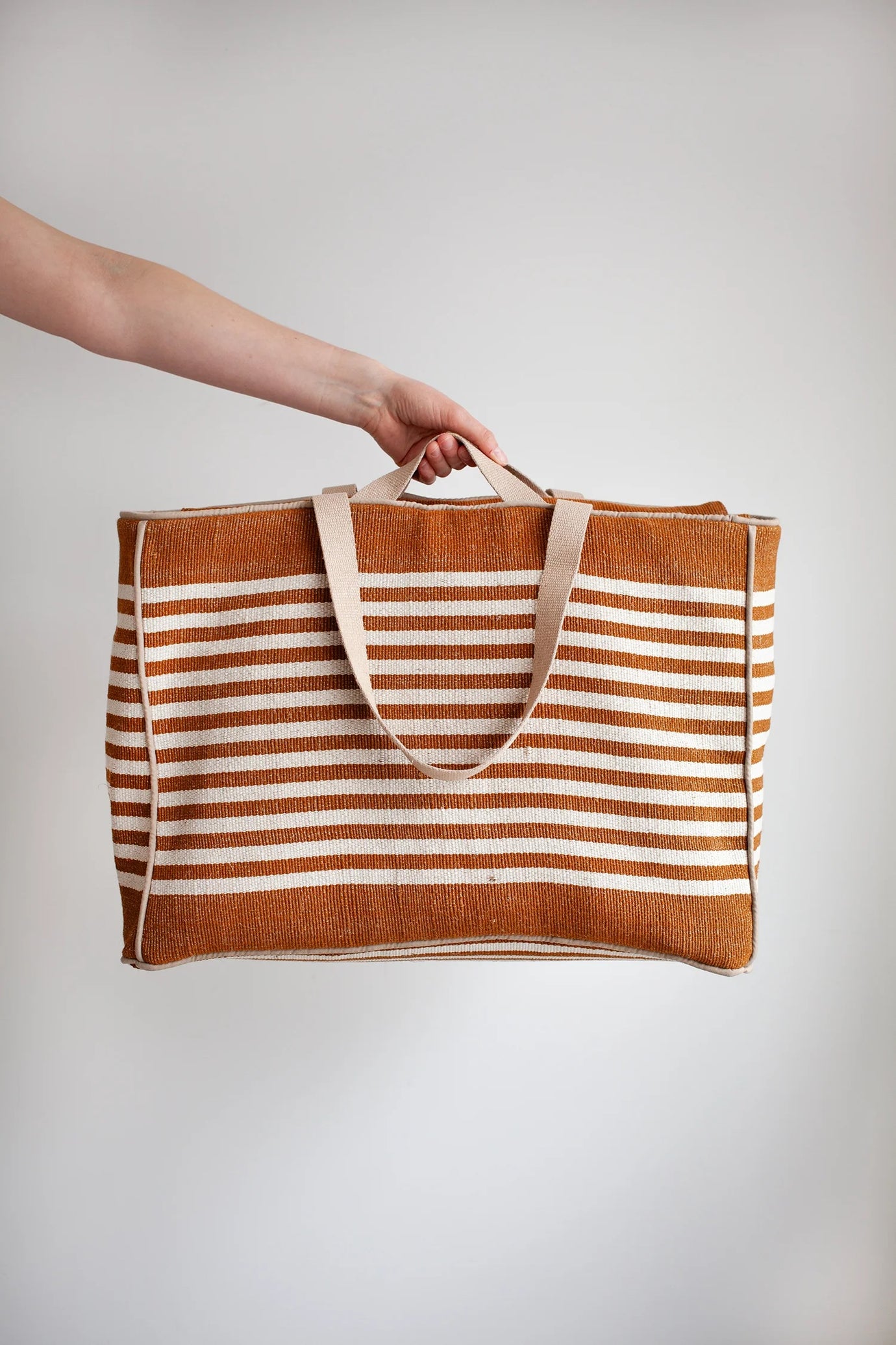 Person holding the Away Tote sewing pattern from the Modern Sewing Co. on The Fold Line. A bag pattern made in cotton canvas or waxed cotton fabric, featuring a roomy interior, lining, internal pockets, zip top, and two handle lengths.