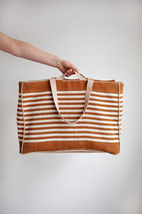 Person holding the Away Tote sewing pattern from the Modern Sewing Co. on The Fold Line. A bag pattern made in cotton canvas or waxed cotton fabric, featuring a roomy interior, lining, internal pockets, zip top, and two handle lengths.