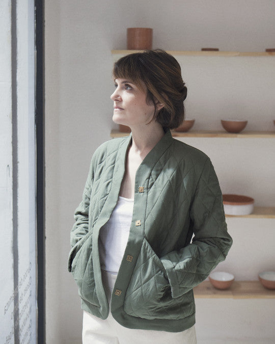 Woman wearing the Ayora Jacket sewing pattern from Pauline Alice on The Fold Line. A reversible quilted jacket pattern made in cotton lawn, linen, viscose, poplin, chambray, or twill fabric, featuring a boxy shape, stand-up collar, long set-in sleeves, big patch pockets, and snap fasteners.